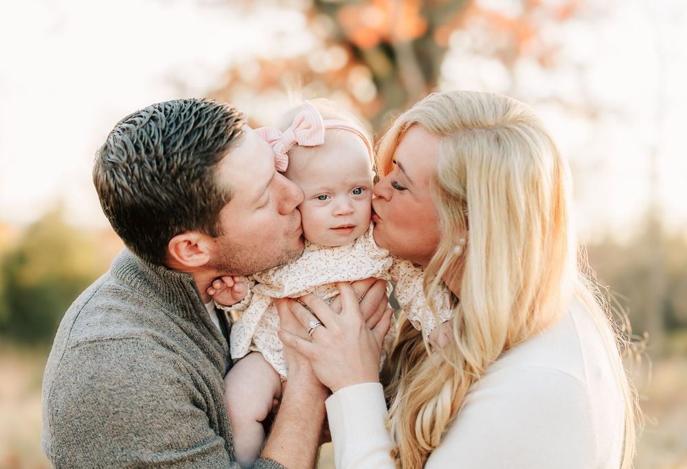 A loving family moment captured at sunset with warm golden light and tender embraces shared between parents and their baby.