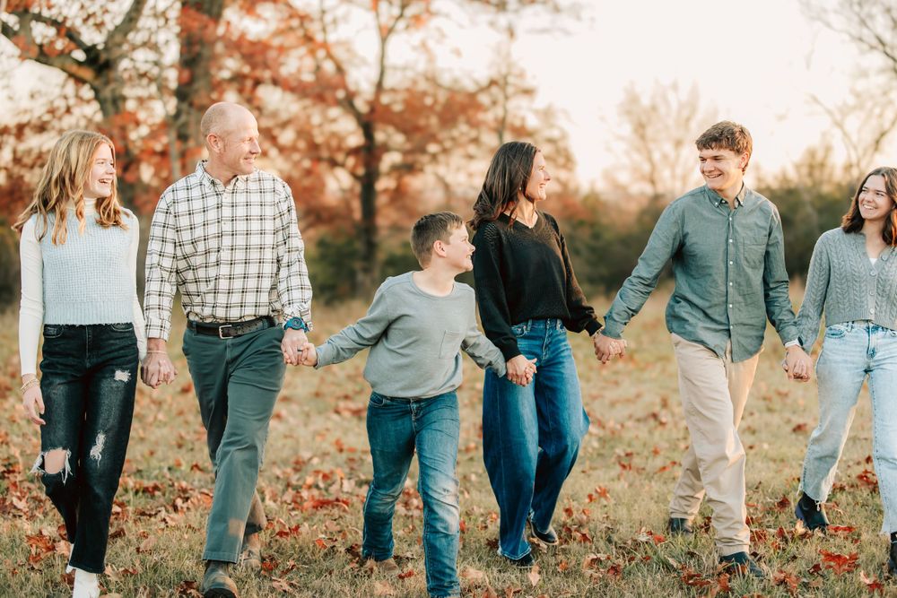 A group of people walking together holding hands in a park during autumn with orange fall foliage in the background.