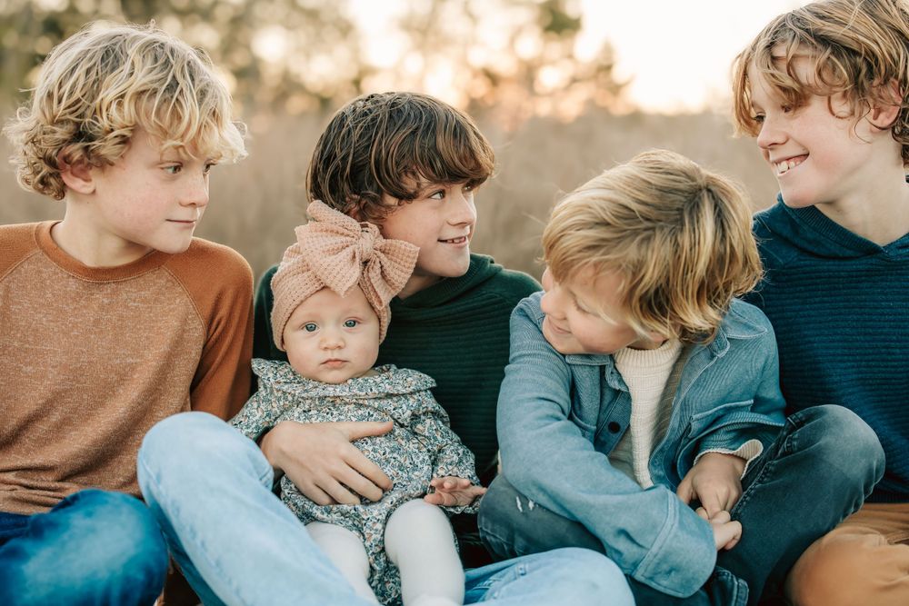 Group of siblings sitting together outdoors wearing casual clothing on a sunny afternoon.
