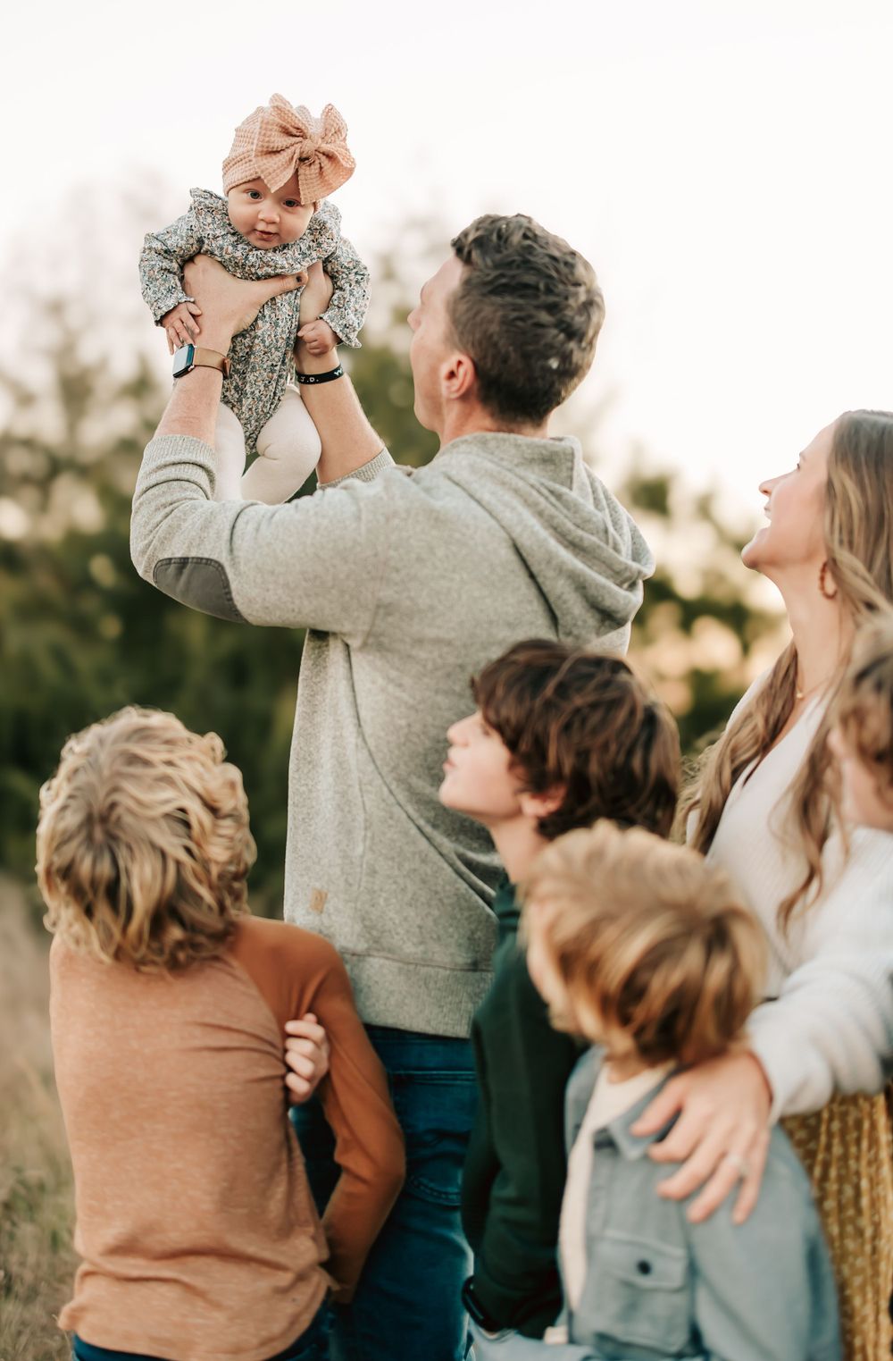 Family standing together outdoors during golden hour sharing a tender moment in casual attire.