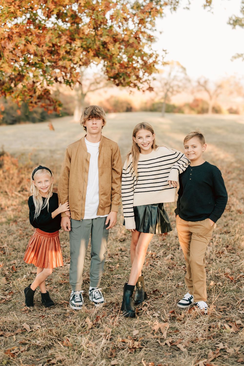 A fall photo capturing people posing together in coordinated casual outfits against autumn foliage and a golden afternoon backdrop.