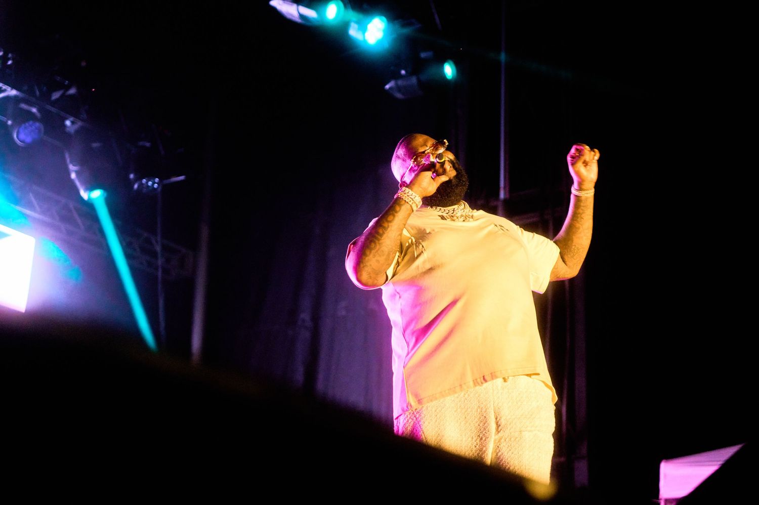 A performer in white clothing stands on stage under dramatic colored lighting during a concert performance.