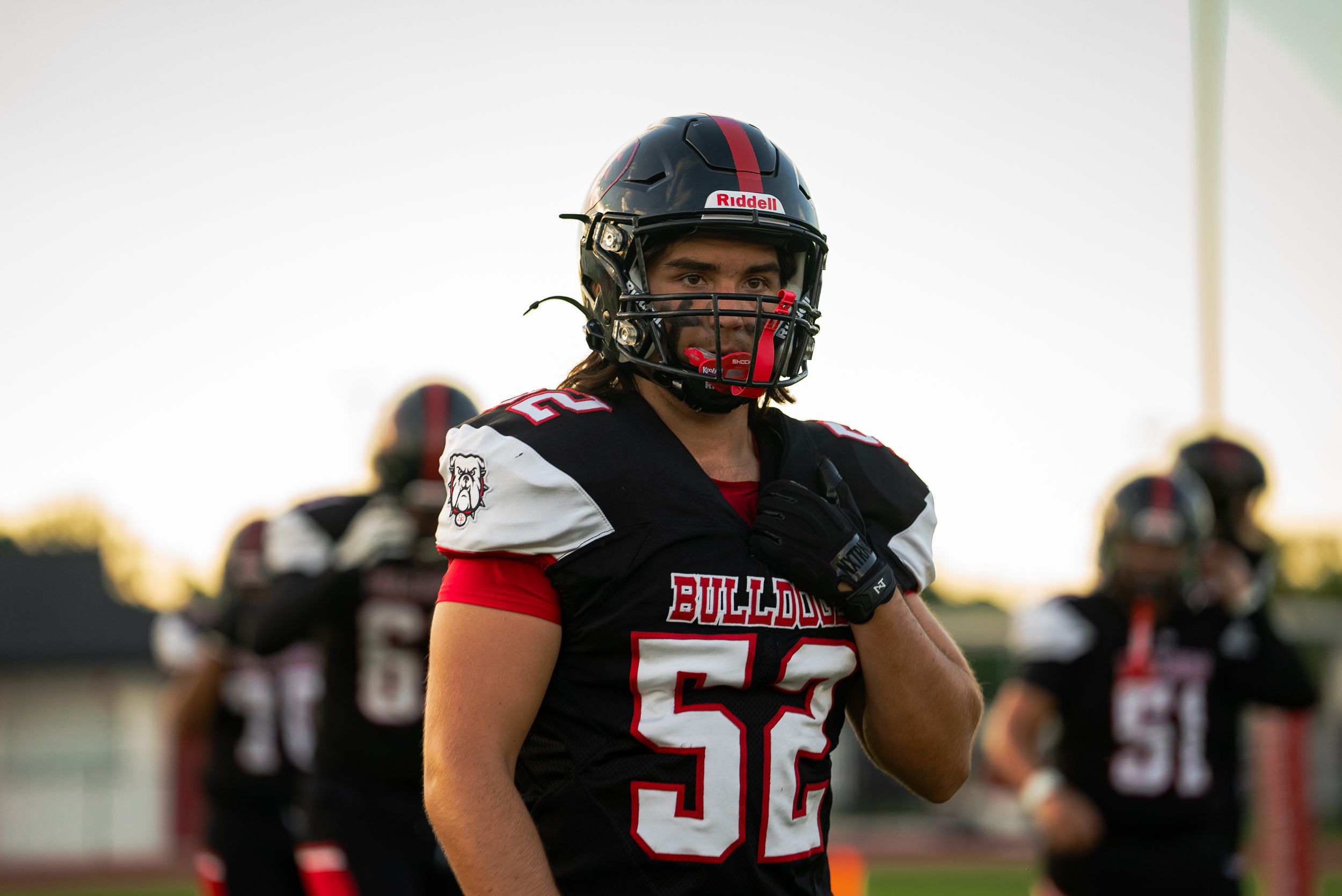 Football player wearing number 56 in black and red uniform stands on field at sunset.