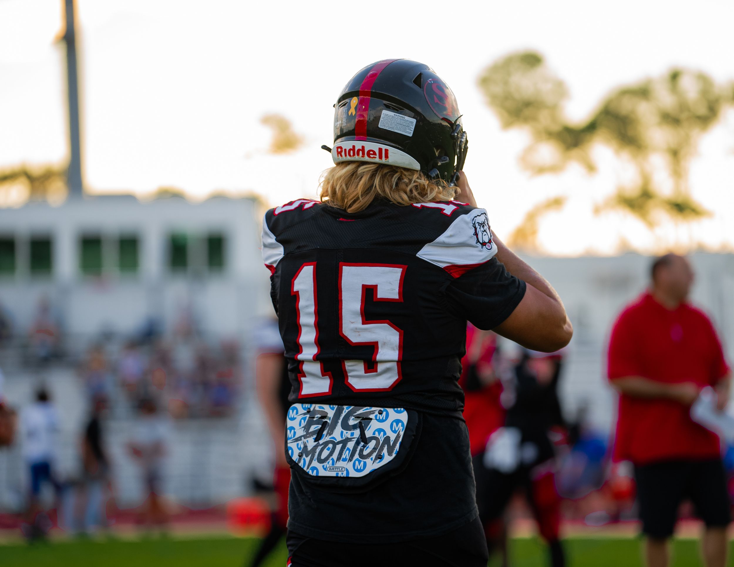 Football player wearing jersey number 15 stands on field at sunset.