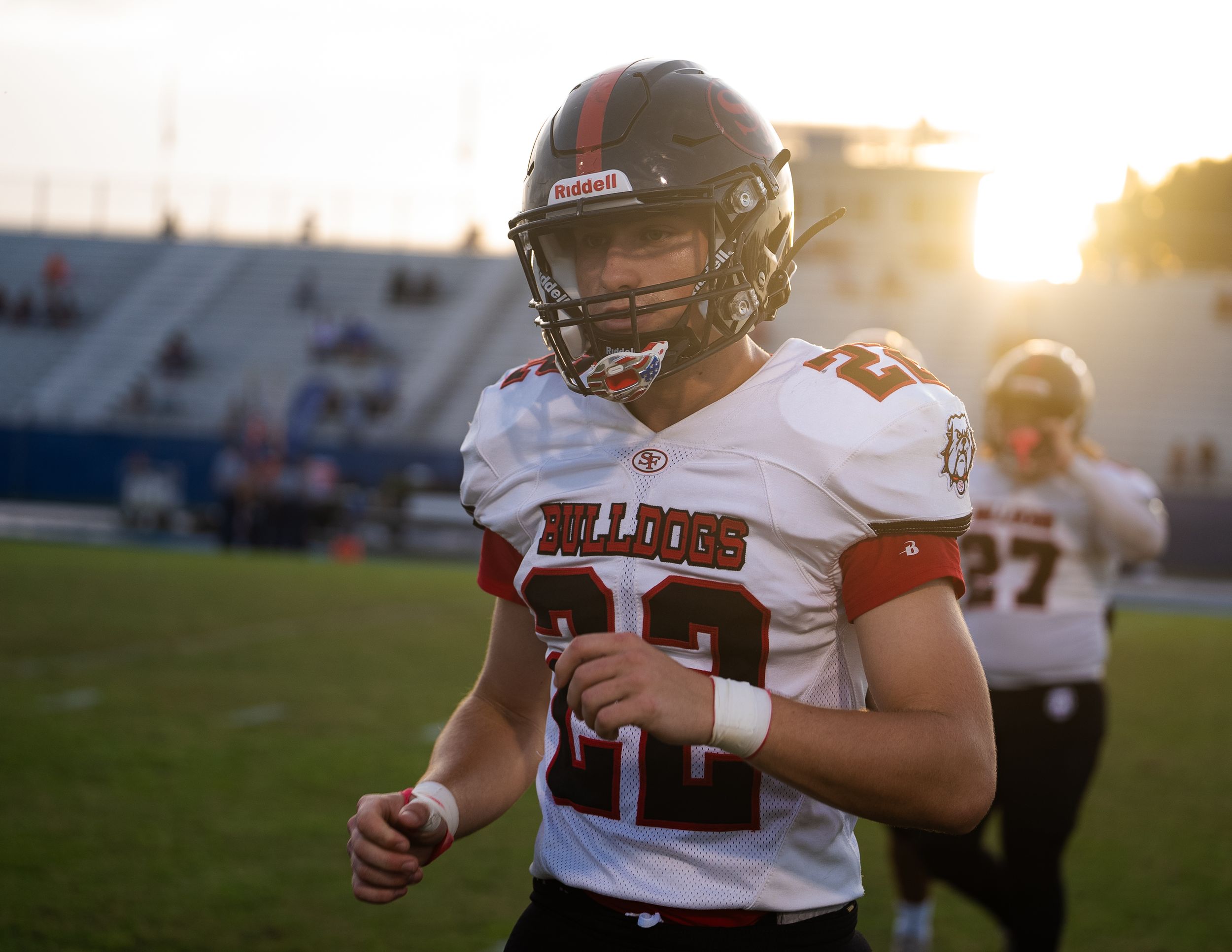 Football player in white jersey number 22 runs on field during golden hour.