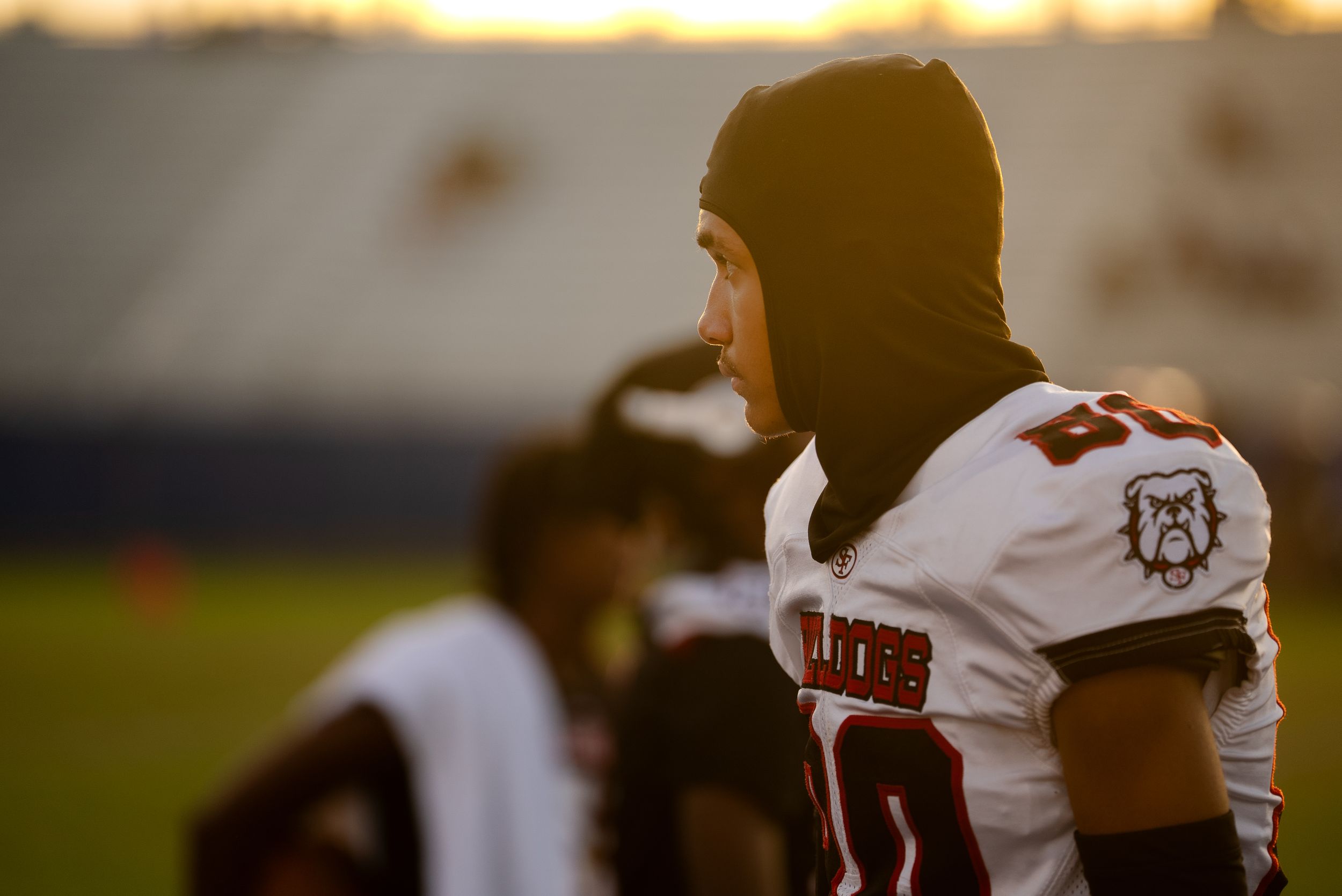 Football player in white uniform and beanie stands on sideline.