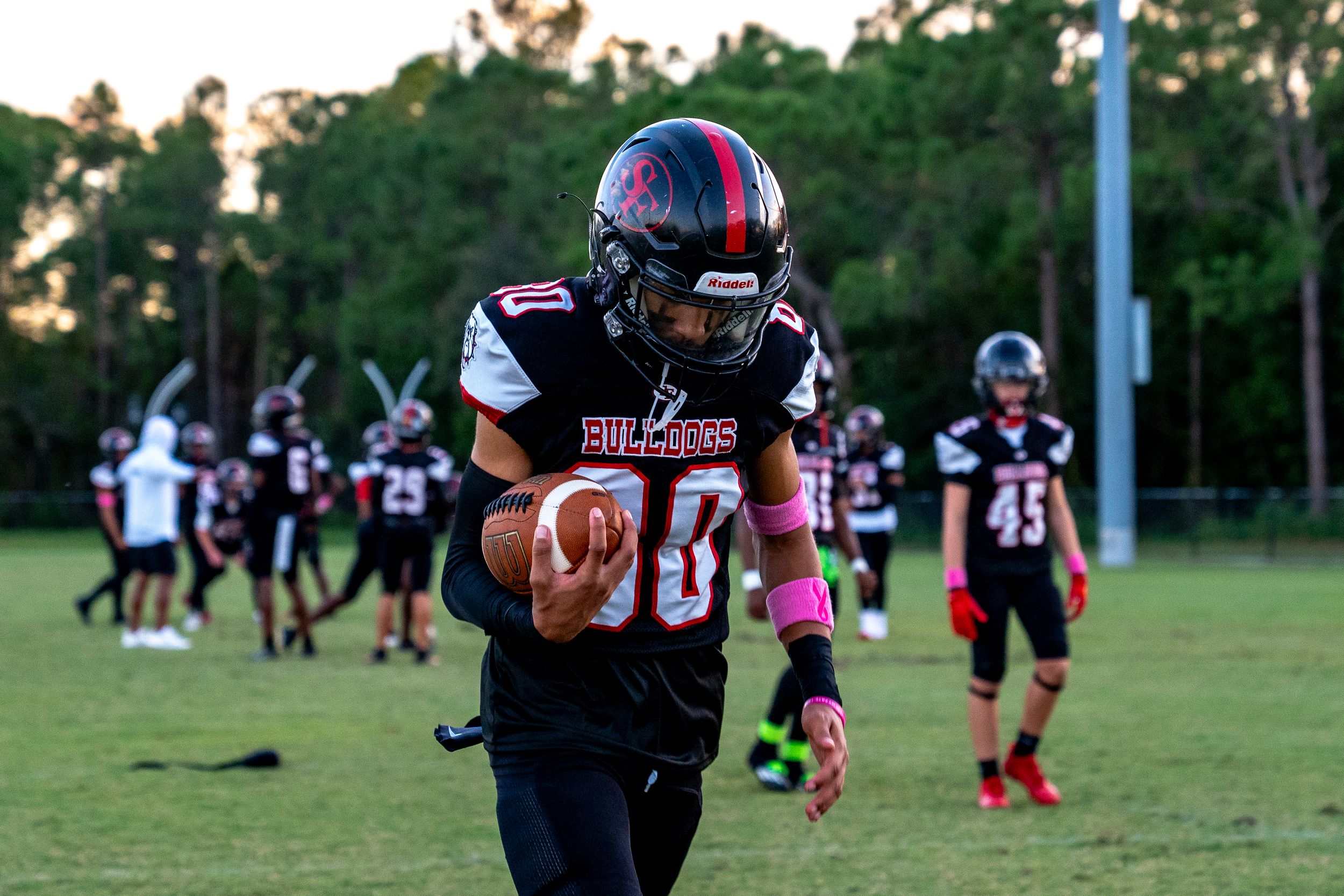 High school football player in black uniform carries ball during practice.
