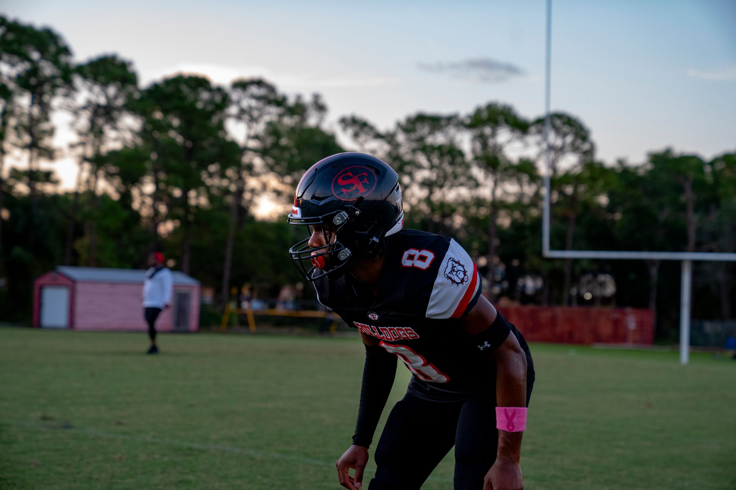 Football player in black uniform on practice field at sunset.