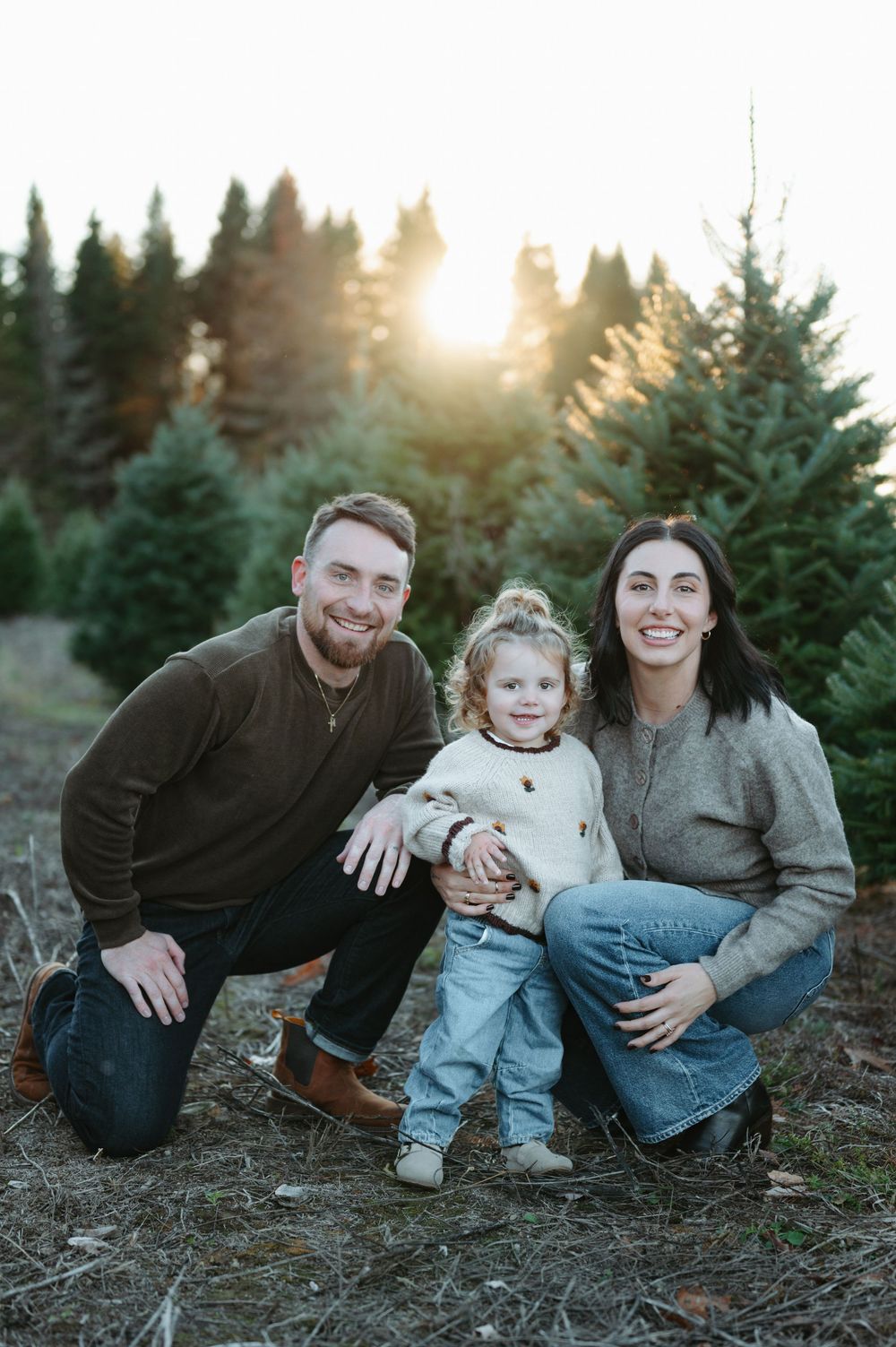 Family of three posing at a Christmas tree farm during golden hour sunset.
