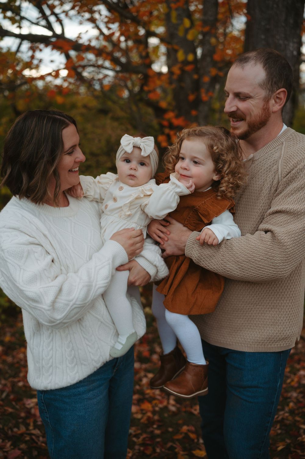 A family enjoys an autumn day together outdoors with fall foliage in the background.
