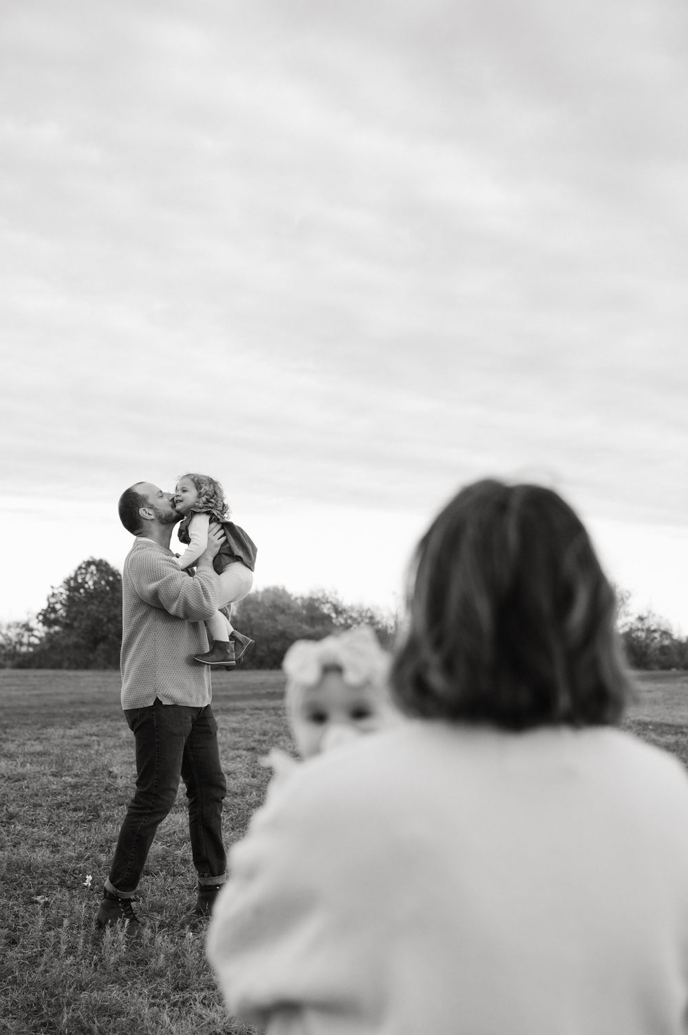 A couple embraces in a tender moment while standing in a misty field at dusk.