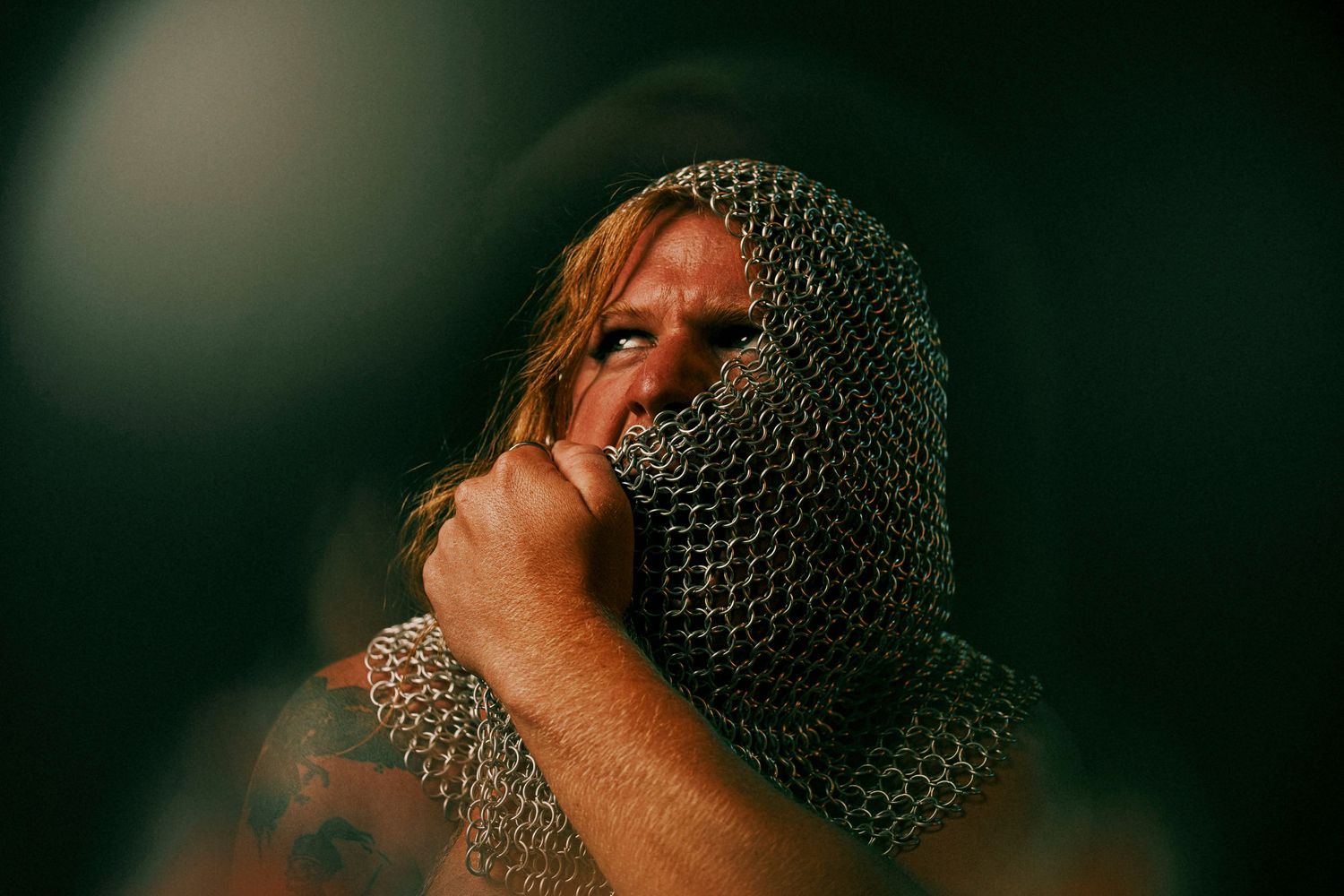 Dramatic portrait with chainmail hood covering face in dark atmospheric lighting.