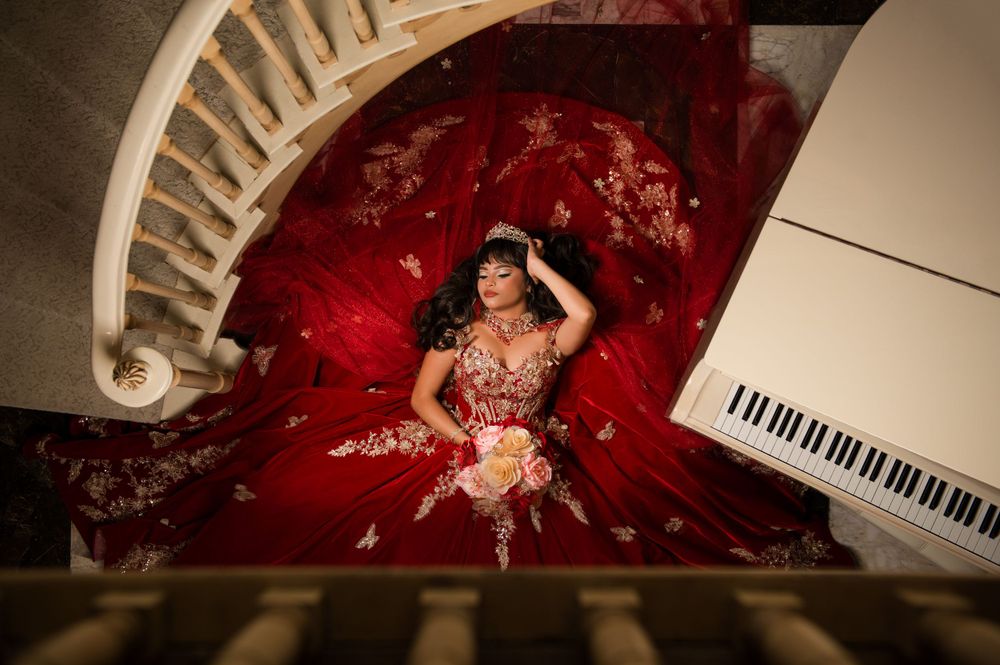 Aerial view of a red quinceañera dress with gold embellishments displayed next to a white grand piano.