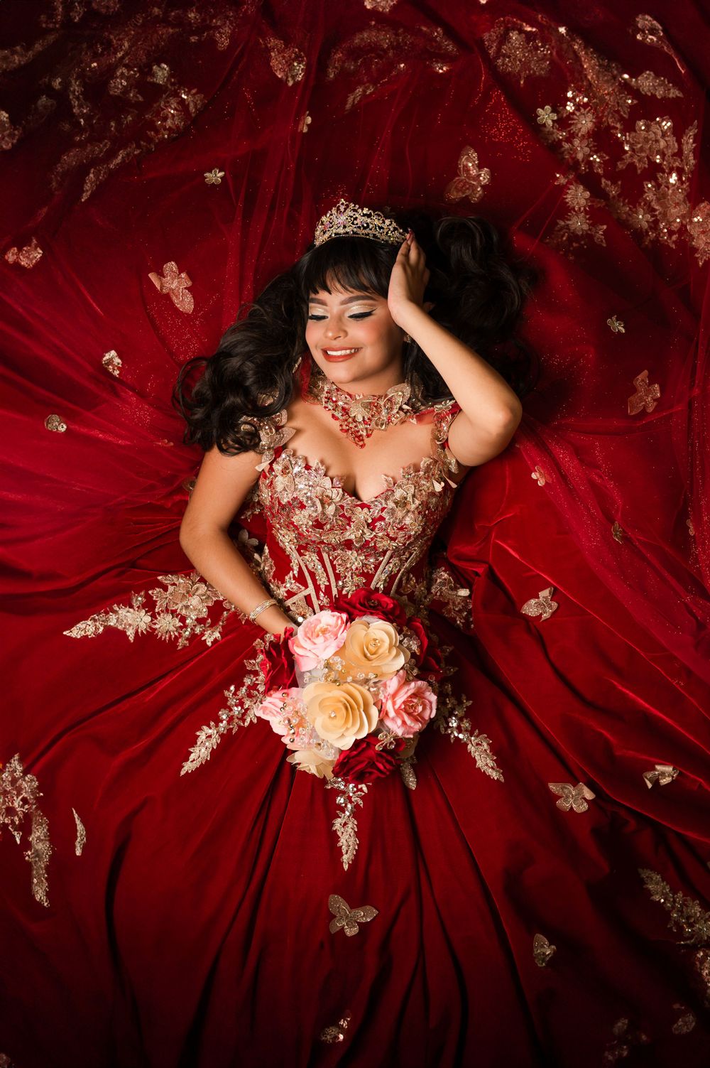 Overhead shot of a stunning red ball gown with intricate gold lace details and pink roses.