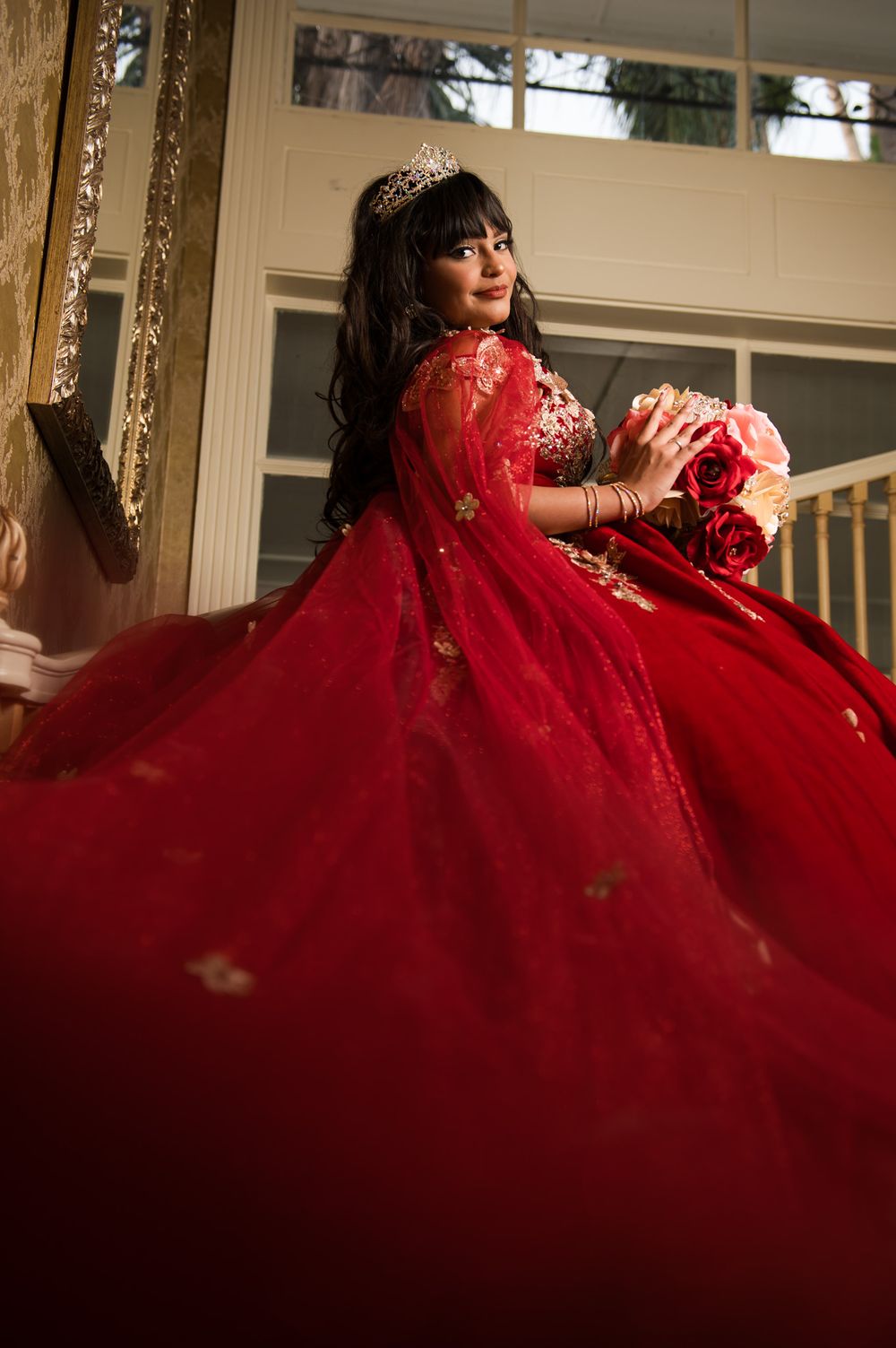 An elaborate red quinceañera gown with embellishments shown in dramatic indoor lighting.