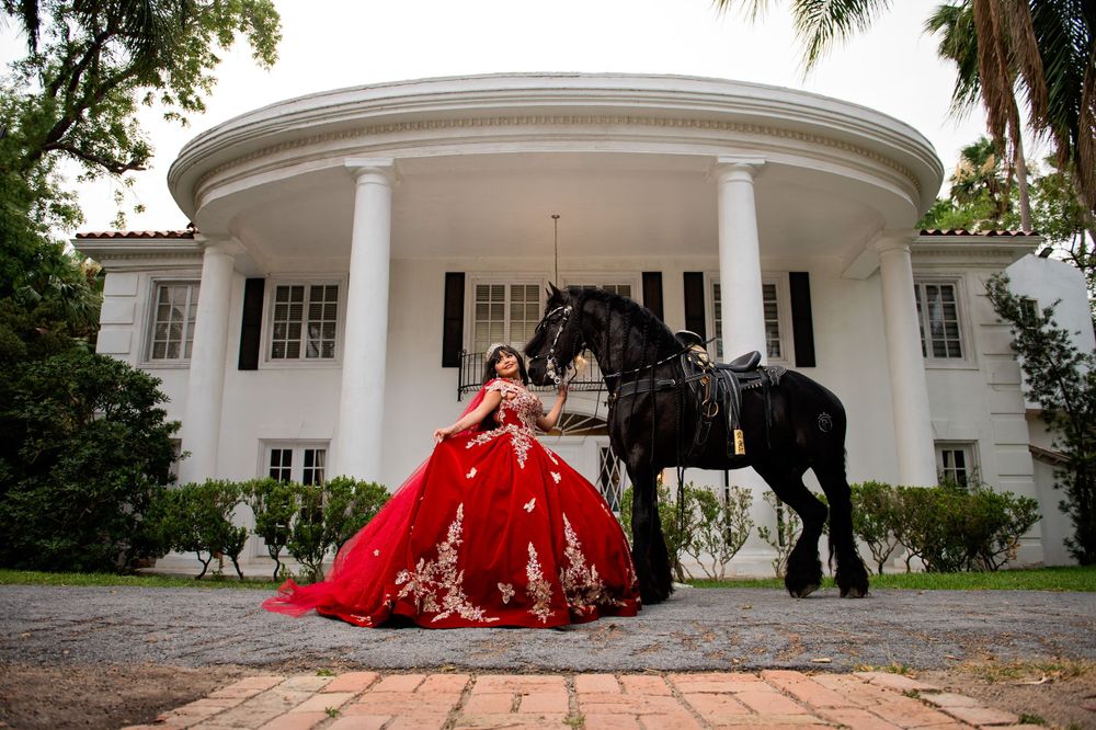 Dramatic red ballgown photographed with a black horse in front of a white columned mansion.