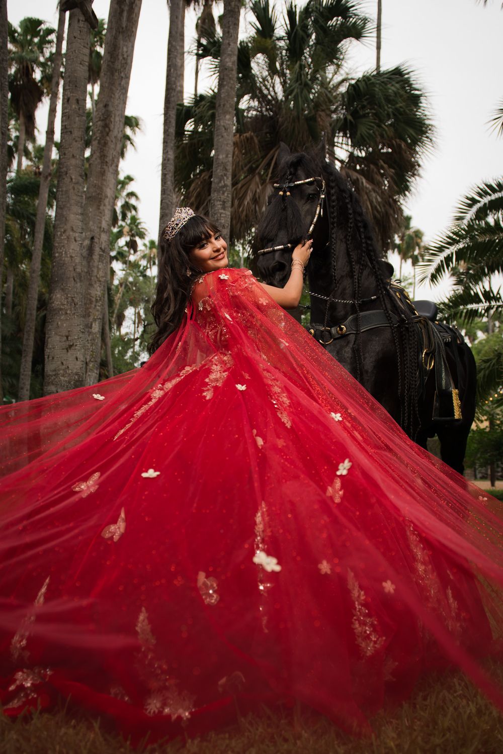 Dramatic red ball gown photographed among palm trees with black horse statue.