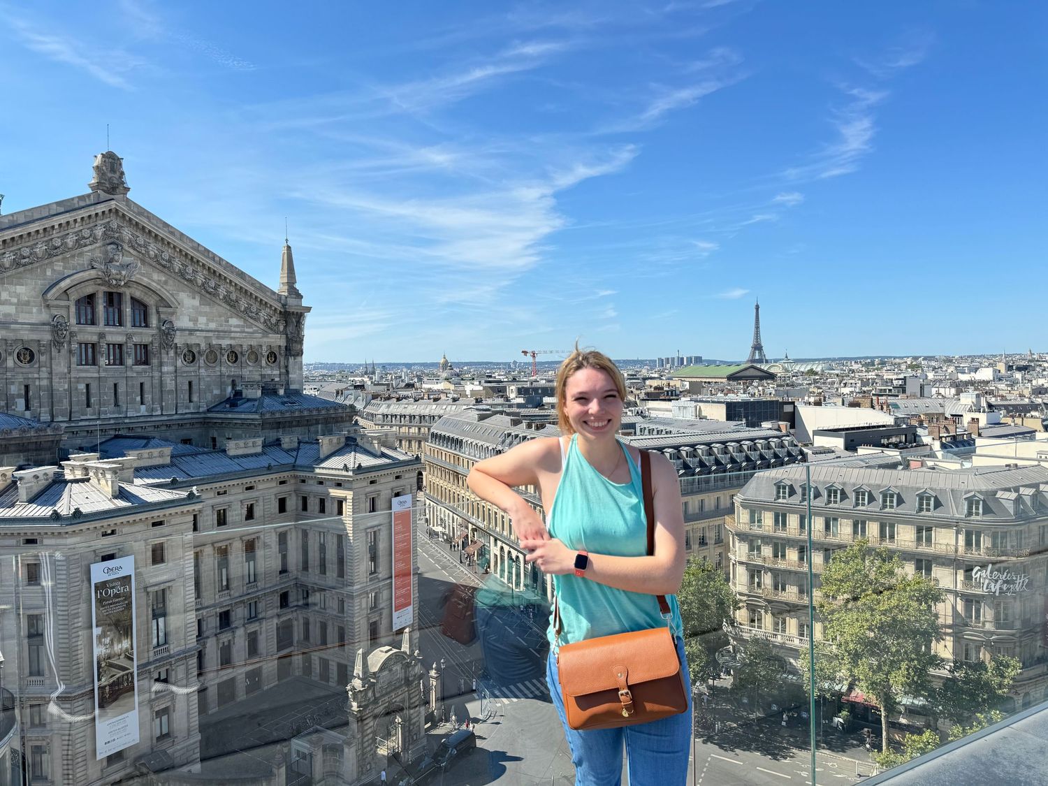 Woman smiling on rooftop terrace in Paris with Eiffel Tower and Opera Garnier in background on sunny day.