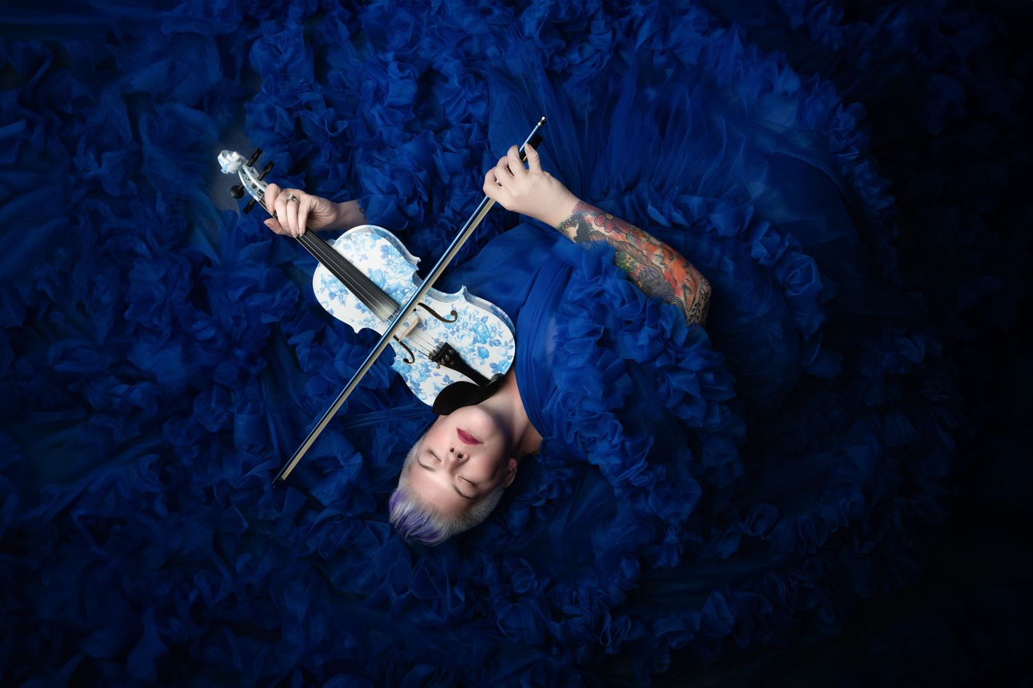 Artistic portrait of a violin player against a deep blue velvet background.