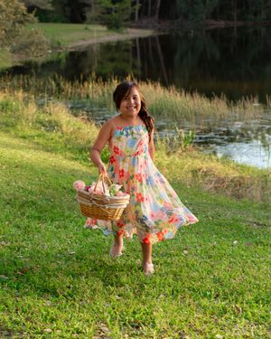 Young girl in floral dress carrying a wicker basket near a pond.
