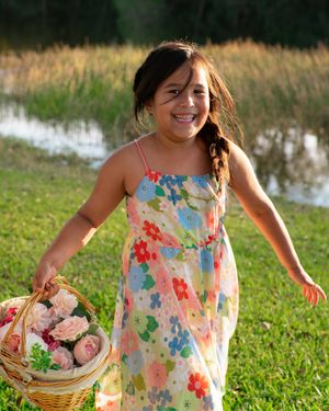 Smiling girl in floral sundress holding a basket of pink roses outdoors.