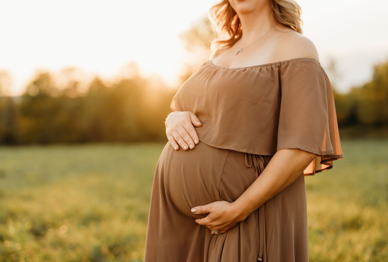 Close-up maternity shot in brown dress during sunset with warm lighting.