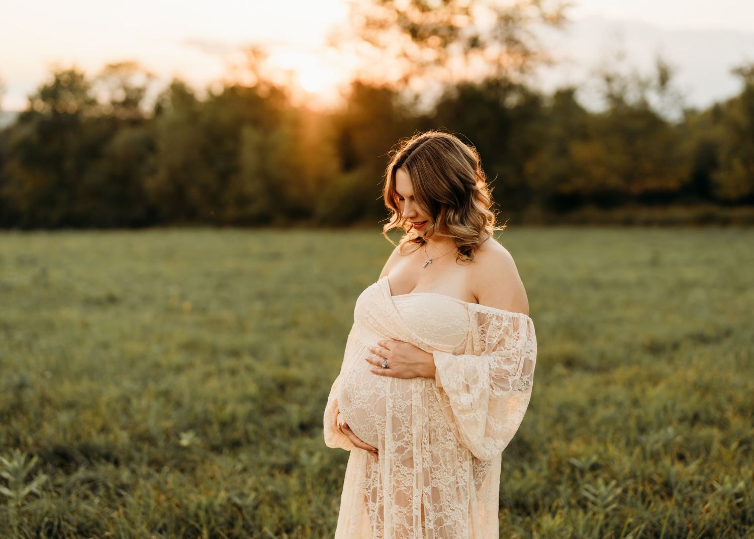 Maternity portrait in lace dress during sunset in grassy field.