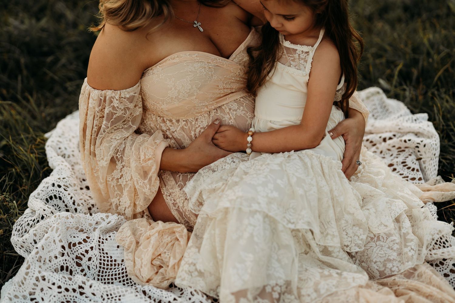 An intimate portrait of two figures in lace dresses sitting together on white lace fabric.