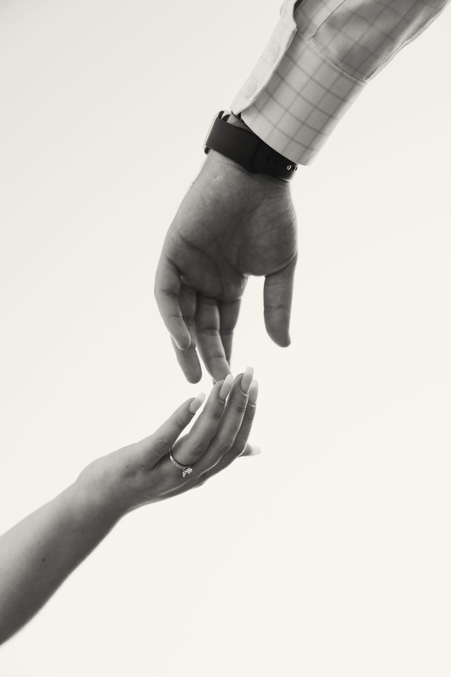 Black and white close-up of two hands reaching toward each other, woman wearing an engagement ring on finger.