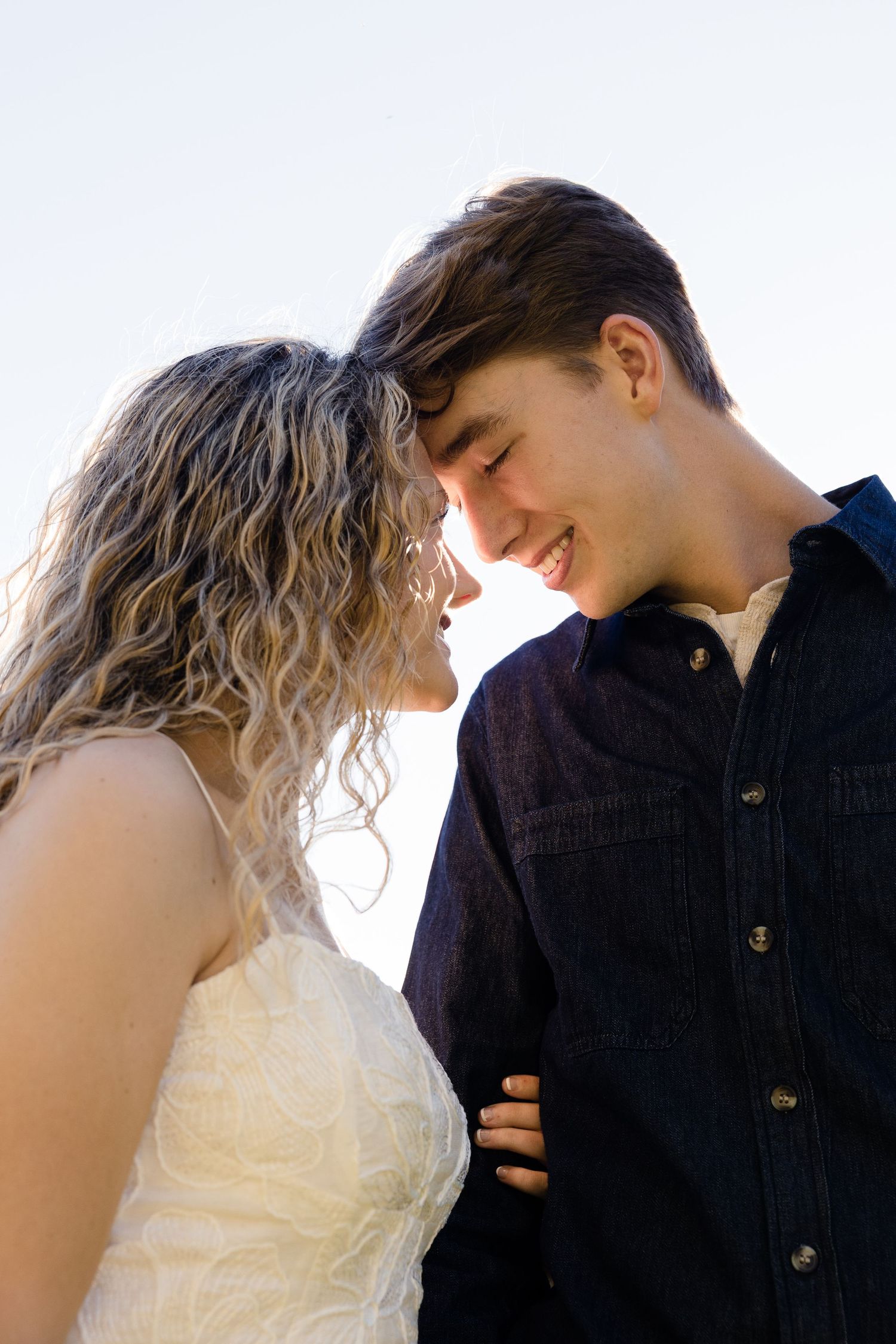 Young couple smiling and touching foreheads against a bright clear sky.