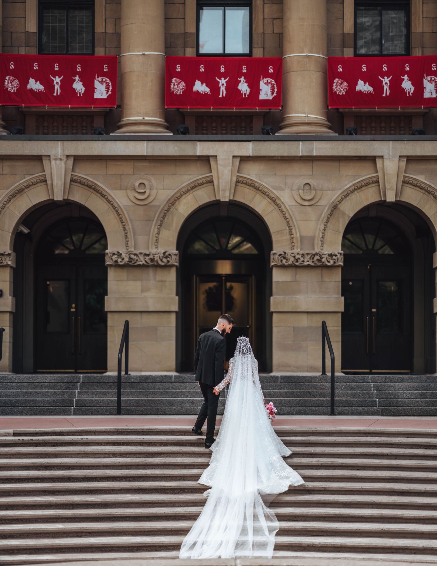 Bride & groom ascend grand city steps, her long train flowing behind. Calgary wedding photography.