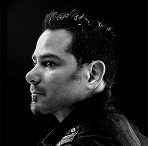A dramatic black and white portrait with side profile lighting featuring a dark leather jacket against a shadowy background.