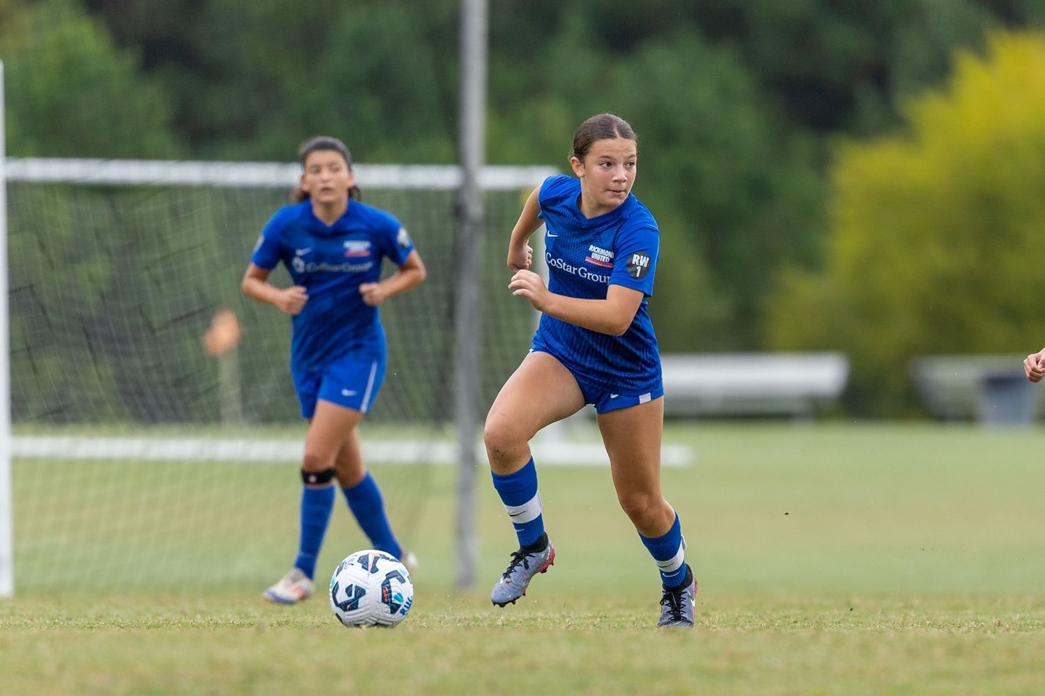 Soccer players in blue jerseys practice defensive moves on a grass field.