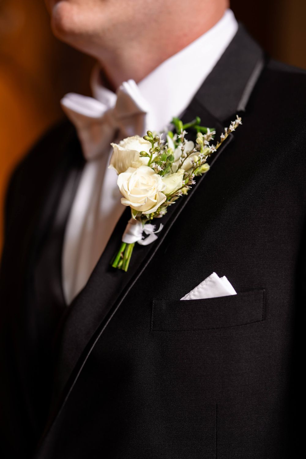 Close-up view of white rose and baby's breath boutonnieres pinned on black suit jackets at a formal event.