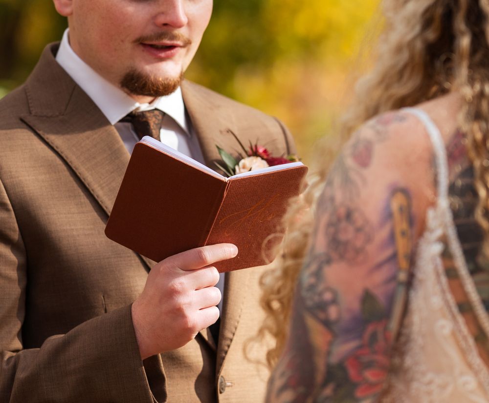 Someone holds a small book while speaking during an outdoor autumn ceremony.