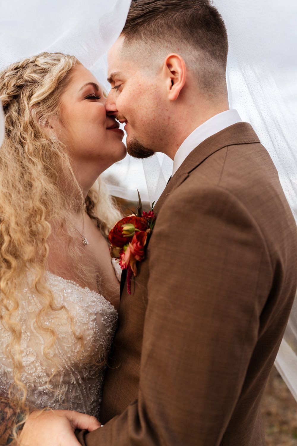 A romantic wedding moment captured as newlyweds share a tender kiss under a white veil.