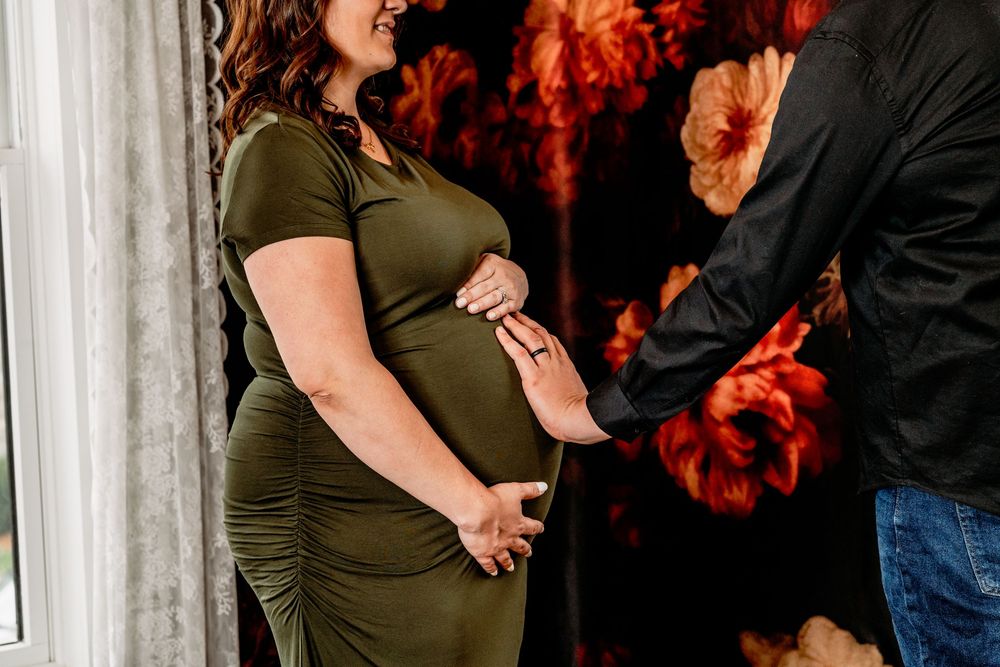 Maternity photo showing pregnant woman in olive green dress against dramatic dark floral background Portrait Photographer West Michigan