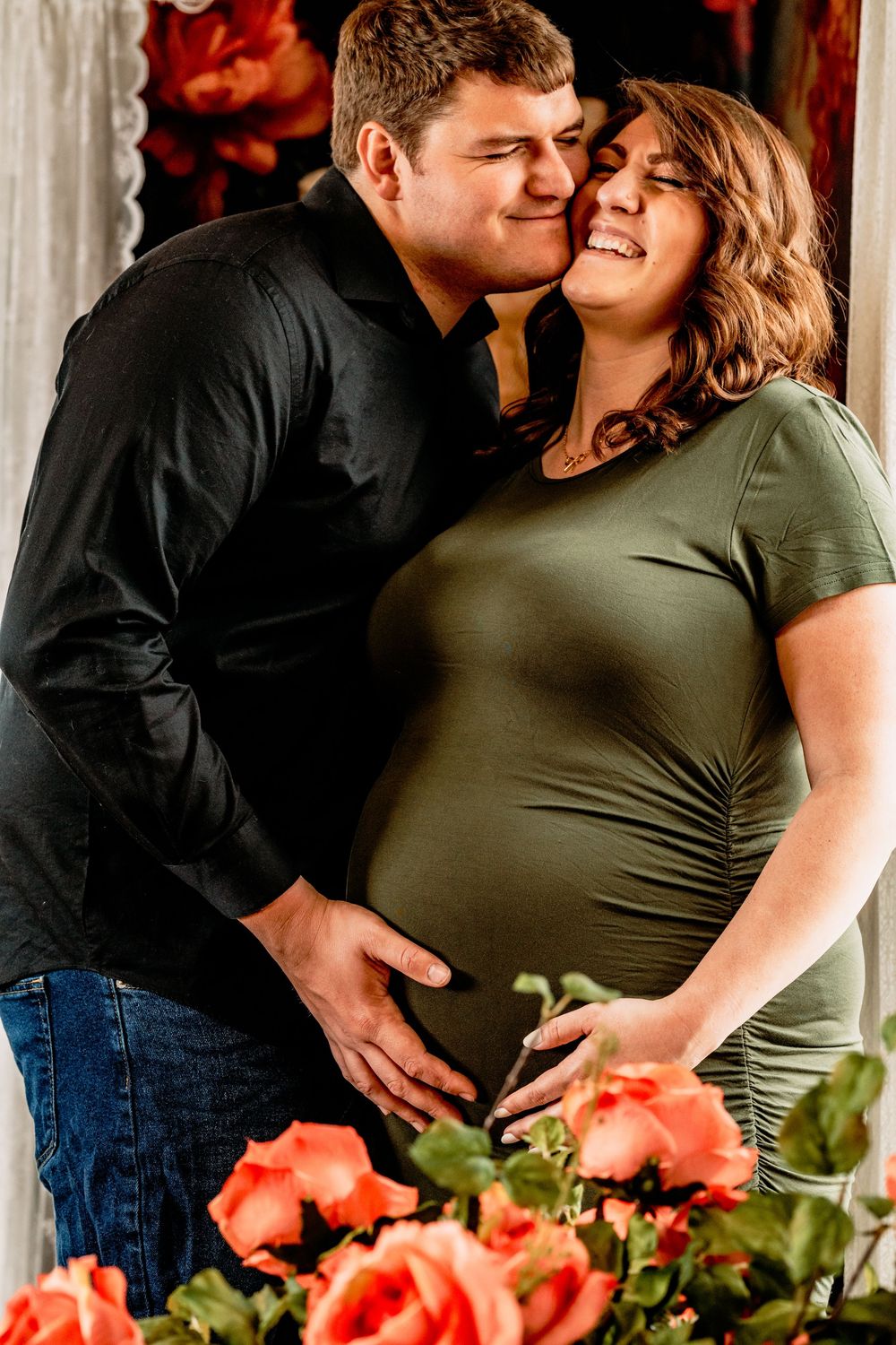 A loving maternity photography session with coral roses decorating the romantic window-lit scene. Photography Sessions, Grand Rapids MI.