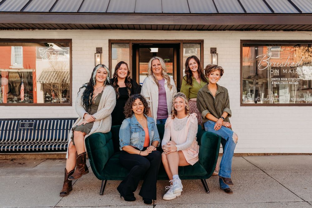 A group of hairstylist sitting and standing together on a bench in front of Brushed On Main Hair Salon On main Street Wayland, MI
