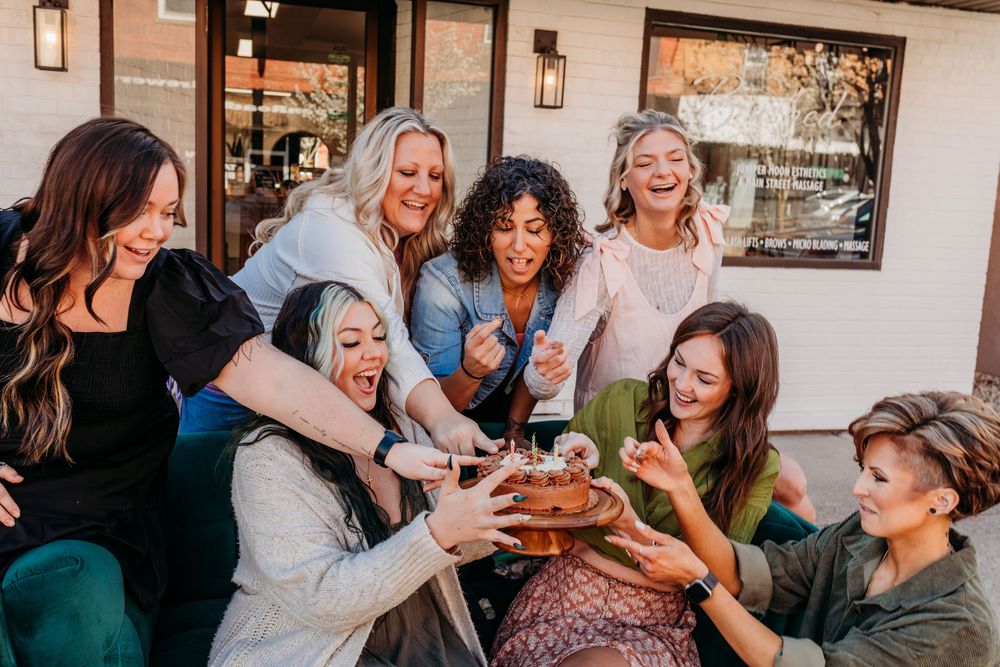 Group of friends laugh together while reaching for shared food at a casual outdoor gathering.  Creative Photographer, Grand Rapids MI