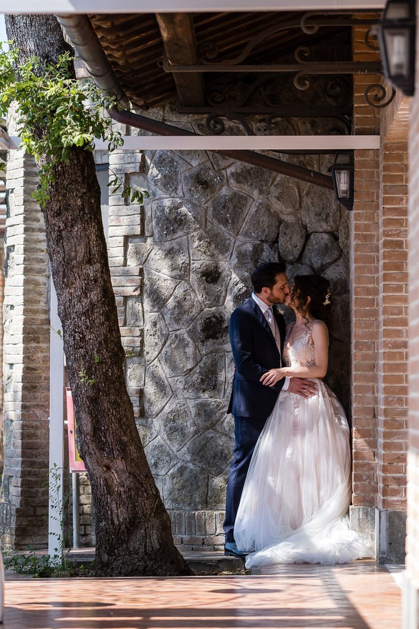 Wedding couple sharing intimate moments under stone archways in an outdoor venue.