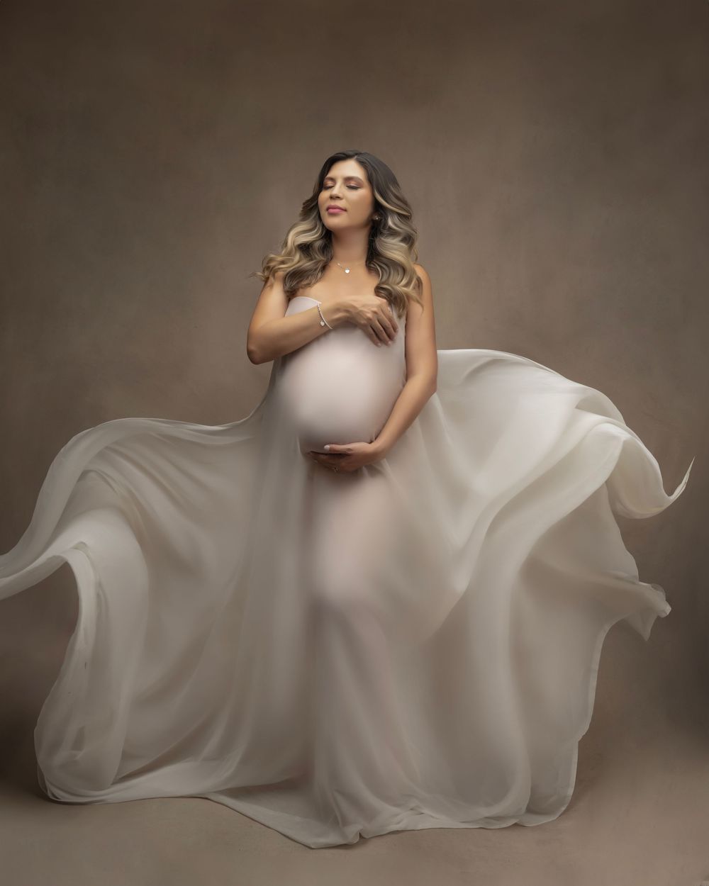 Elegant maternity photo featuring billowing white dress against dark backdrop.