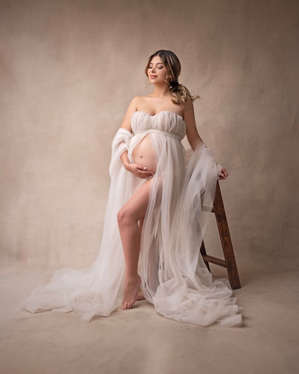 Gentle maternity portraits with flowing white fabric and natural poses on brown background.