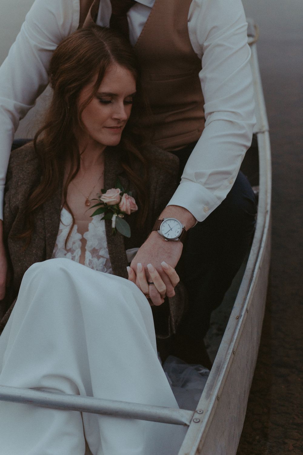 Romantic wedding moment showing couple holding hands with bride in white dress holding roses in moody natural lighting.