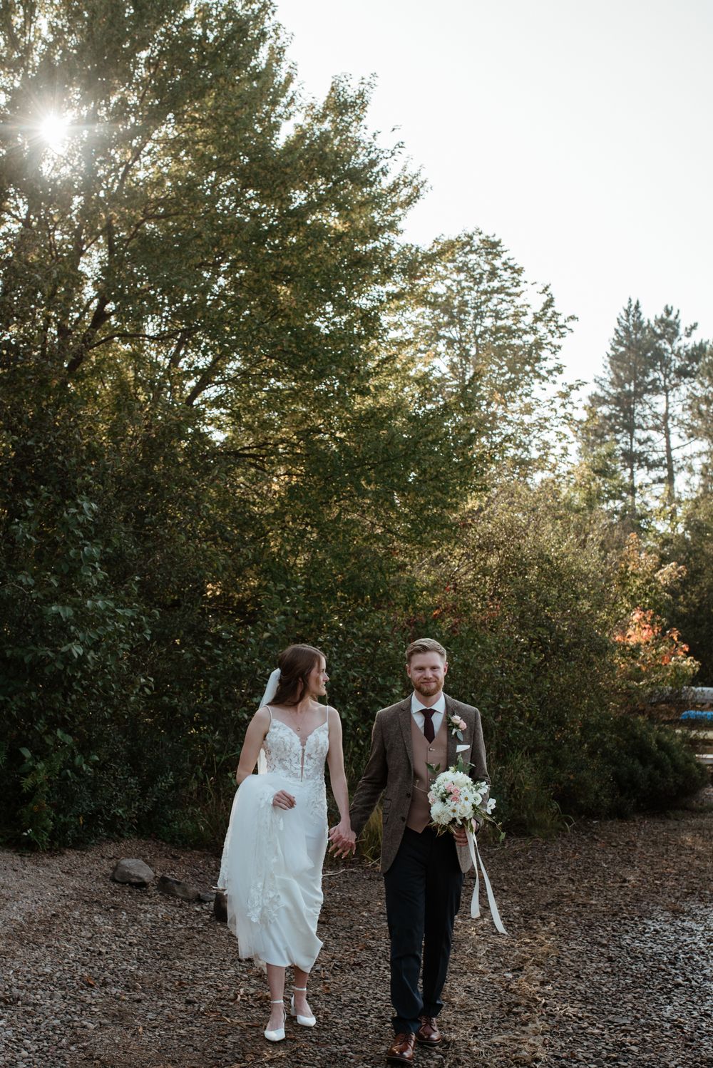 A couple strolls together on a wooded path during golden hour as sunlight filters through autumn trees.