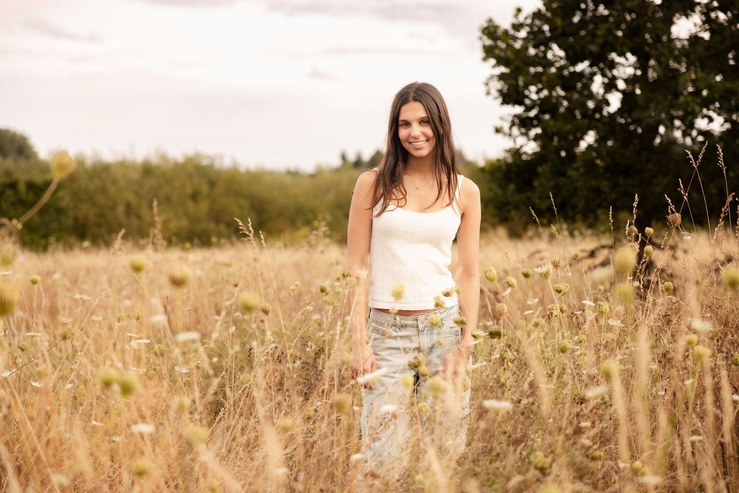 A person in a white tank top stands in a tall grass field at sunset during golden hour.