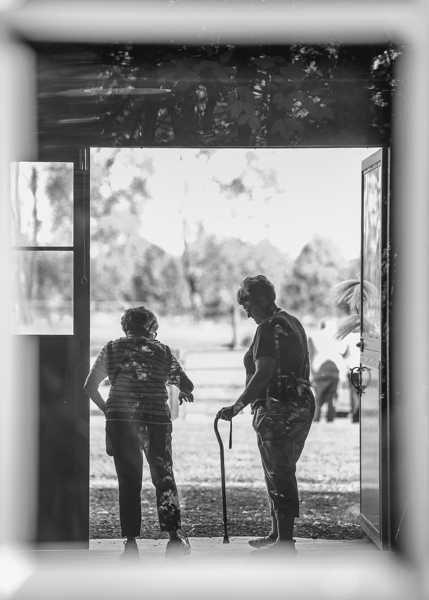 Two silhouettes standing in a doorway looking out into bright daylight.