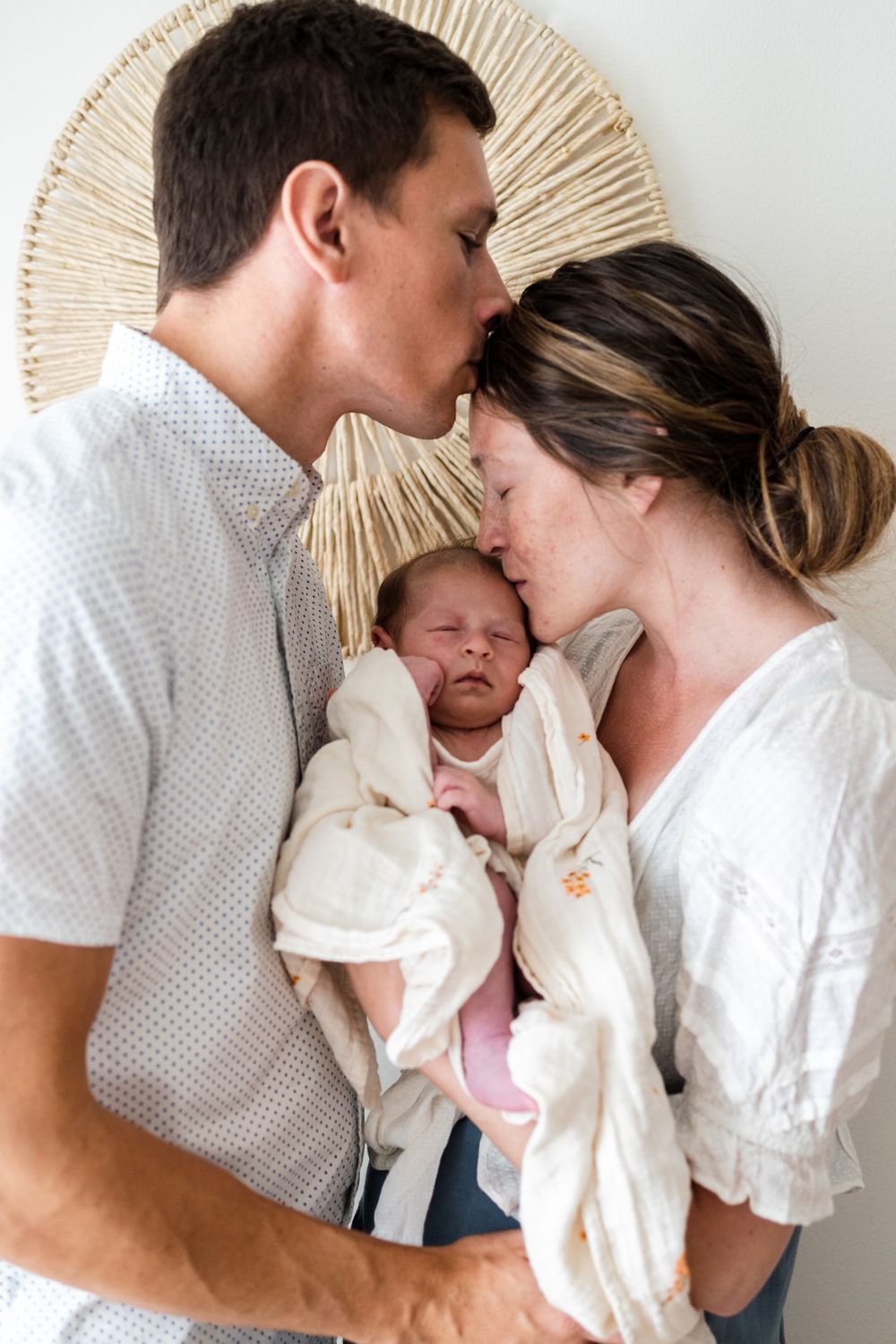 Series of tender family moments showing parents sharing loving kisses with their newborn baby against a sunburst wall decor.