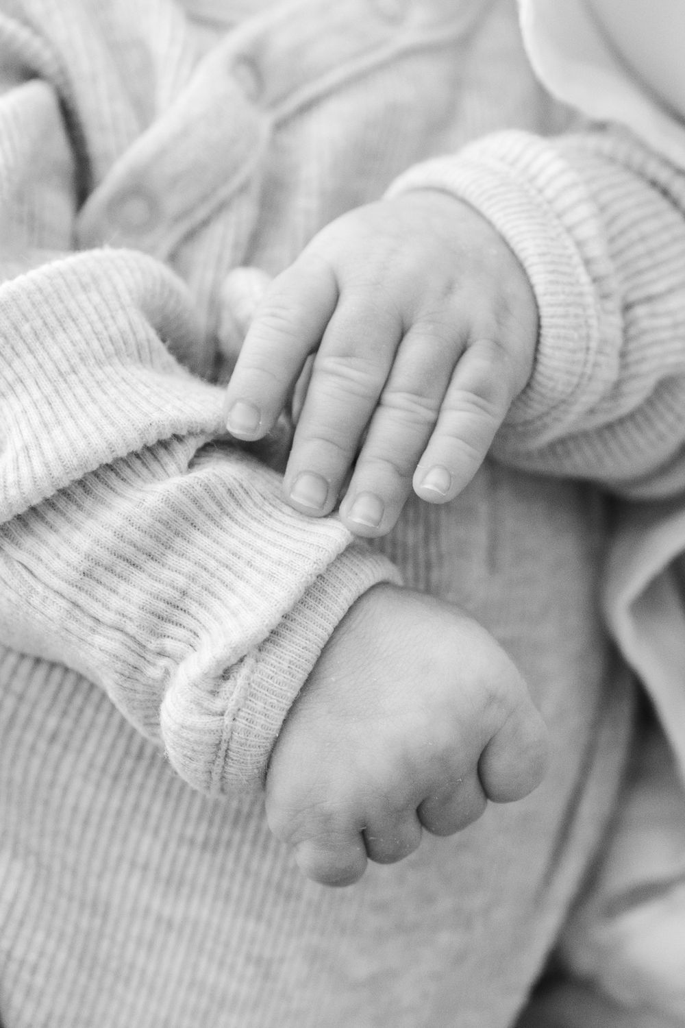 A close-up black and white photo series showing a baby's tiny hands grasping and reaching in soft knit fabric.