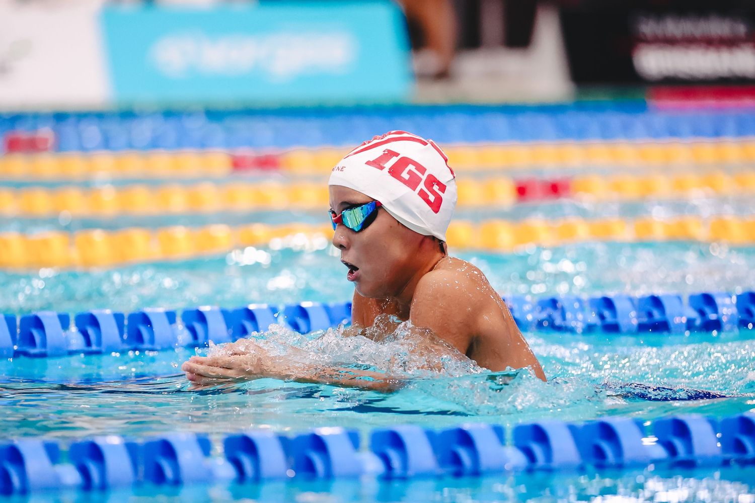 Competitive swimmer wearing red and white cap performs breaststroke in pool during race.